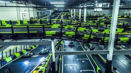 Pista de kart coberta em dois andares, com barreiras verde-limão, placa «SLOW» e pilotos de capacete em karts na reta de largada numerada; foto do acervo do site, ligada ao Andretti Kart