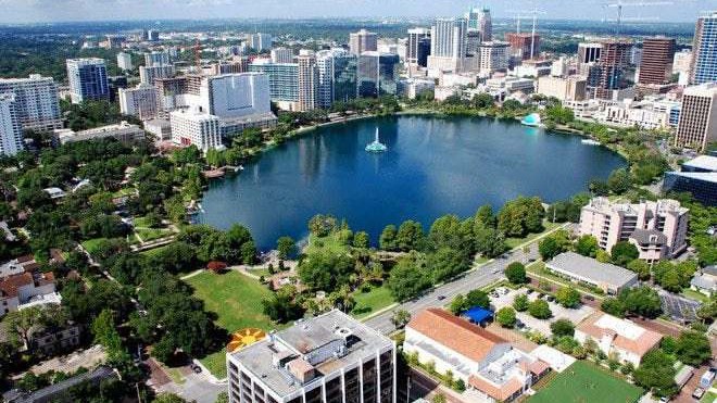 Vista aérea do Lake Eola, o lago redondo cercado de árvores no centro de Orlando, com a fonte no meio da água e os prédios do centro em volta
