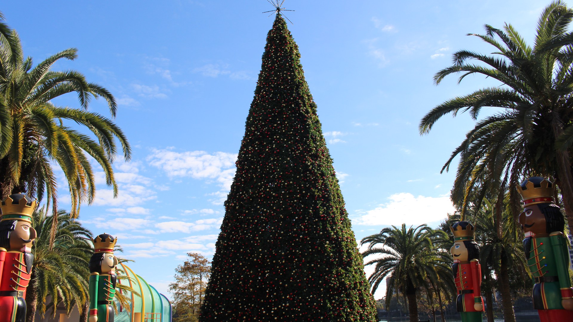 Árvore de Natal alta e cônica, coberta de bolas vermelhas e douradas, no Lake Eola Park, em Orlando, entre palmeiras e bonecos gigantes de soldadinho de chumbo, sob céu azul