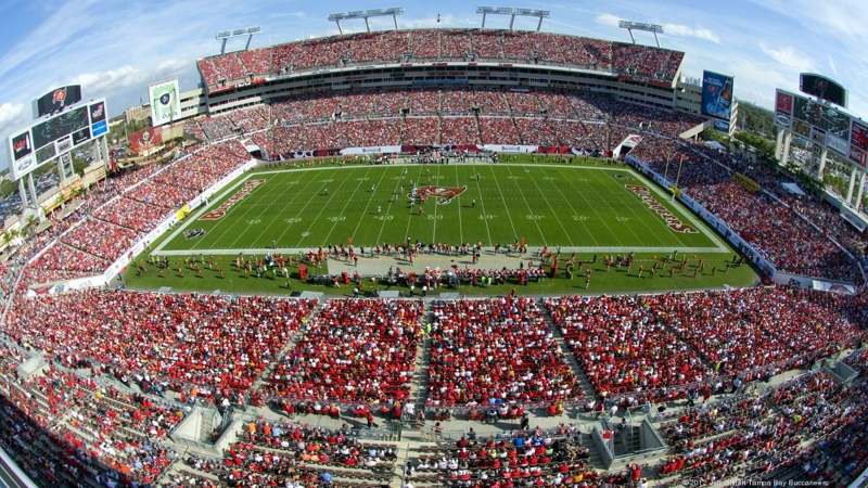 Vista do alto do Raymond James Stadium, em Tampa, lotado de torcedores de vermelho em dia de jogo dos Buccaneers, com o gramado e o logo do time no centro do campo